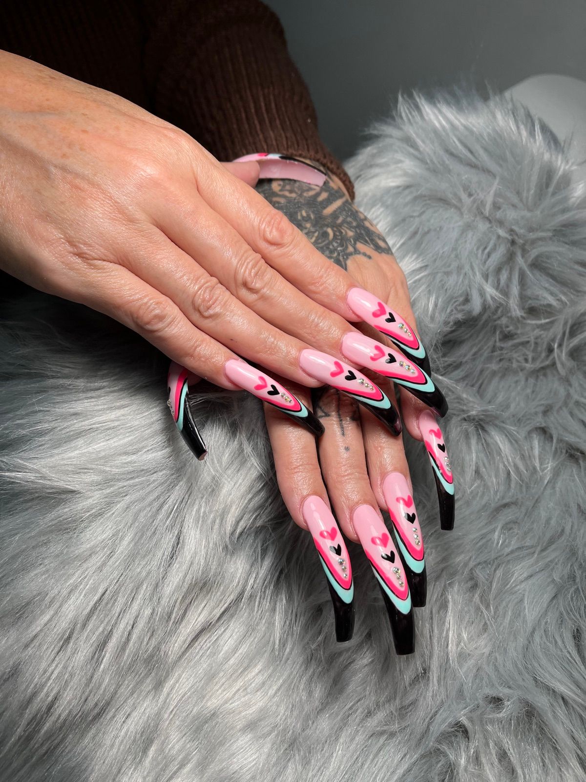 Extra-long pink coffin nails with black and teal French tips and hearts
